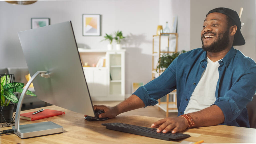 Ritratto dell'uomo afroamericano felice che ride al video che ha guardato sul suo personal computer a casa. - Foto, immagini