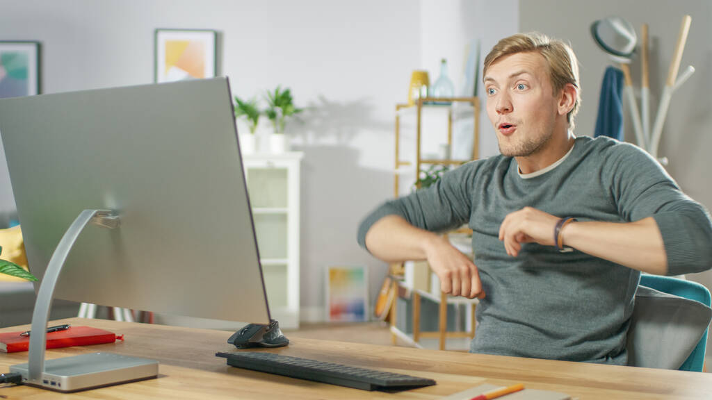 Portrait of Surprised Handsome Man Working on Personal Computer Has Stroke of Luck, Emotionally Showing it. In the Background Stylish Cozy Living Room. - Photo, Image