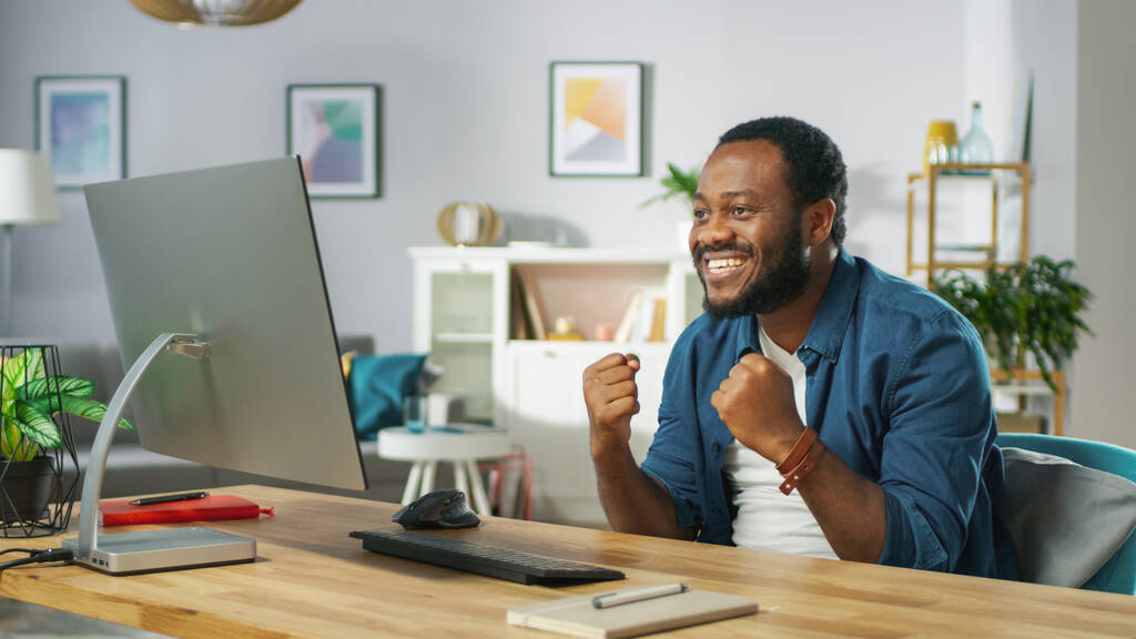 Izgatott fiatalember használ személyi számítógép otthon, nyer nagy, nem "igen" gesztus, ünnepli győzelem érzelmileg. A háttérben Hangulatos nappali. - Fotó, kép
