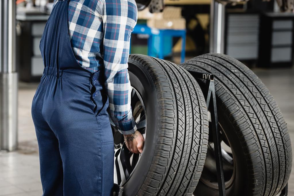 partial view of mechanic in overalls taking car wheel in workshop - Photo, Image