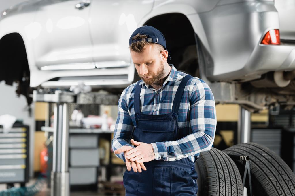 technician rubbing hands near auto raised on car lift on blurred background - Photo, Image