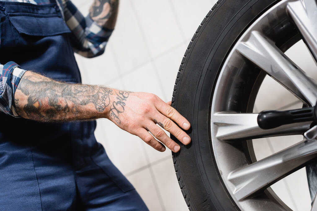 partial view of tattooed technician touching car wheel in workshop on blurred background - Photo, Image