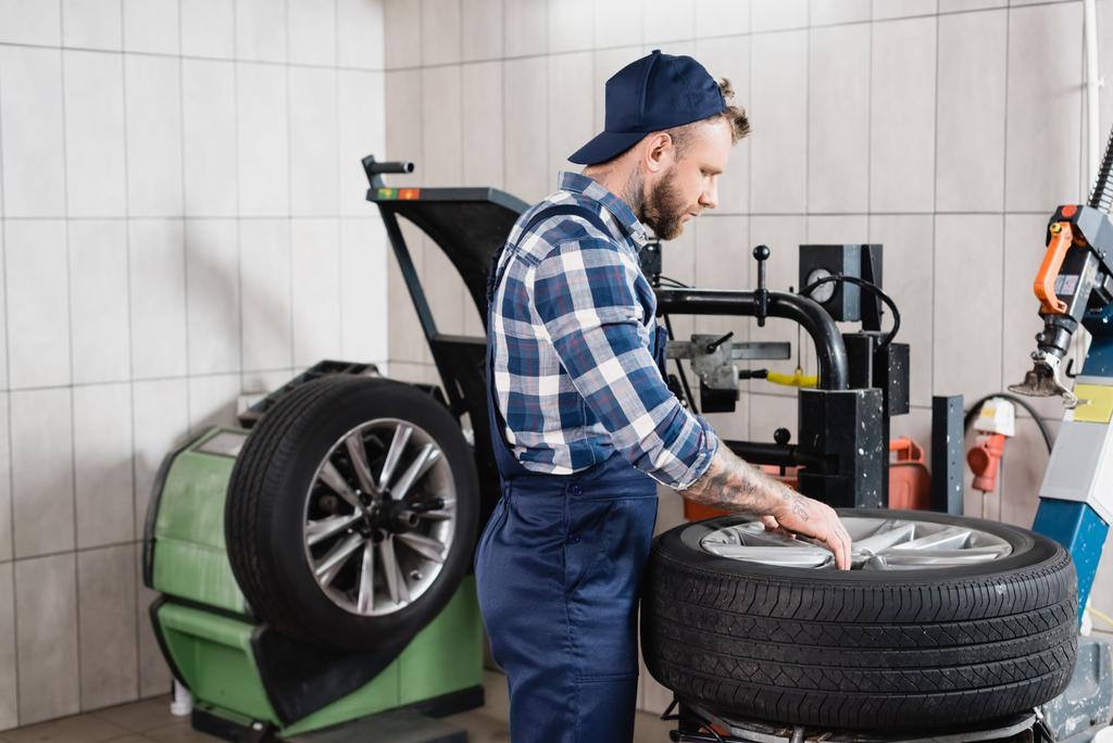 reparador en overoles poner rueda en cambiador de neumáticos en taller - Foto, Imagen