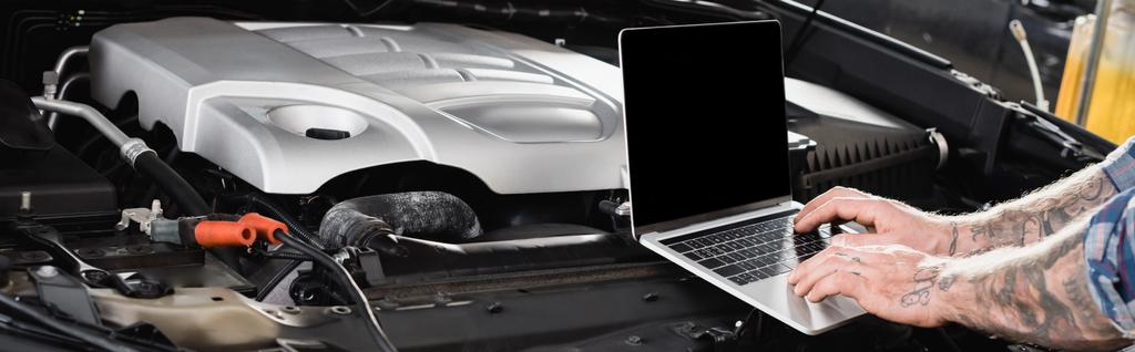 przycięty widok wytatuowanego mechanika, diagnostyka samochodu na laptopie w pobliżu komory silnika, baner - Zdjęcie, obraz