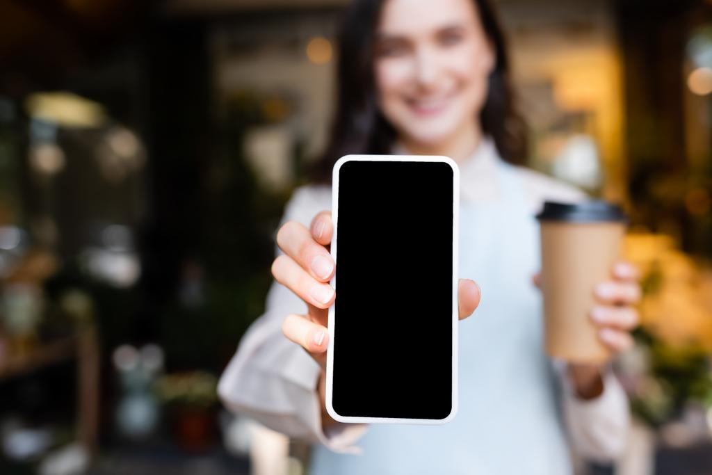 mladá květinářka drží smartphone s prázdnou obrazovkou a kávou jít na rozmazané pozadí - Fotografie, Obrázek