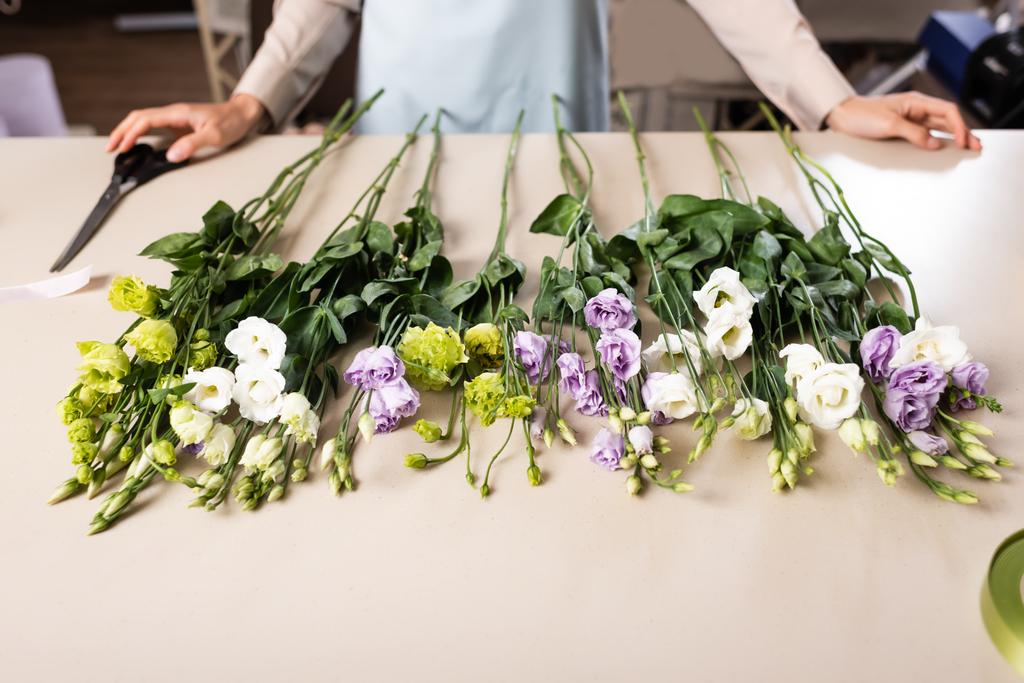 vista recortada de floristería cerca de flores eustoma en la mesa en la tienda de flores sobre fondo borroso - Foto, Imagen
