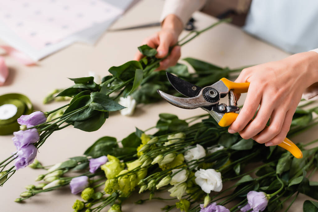 bijgesneden weergave van bloemist houden snoeischaar en eustoma bloemen, terwijl het maken van boeket op wazig voorgrond - Foto, afbeelding