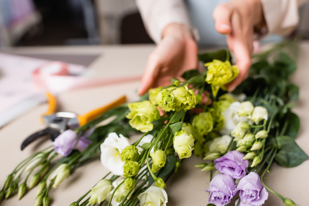 частичный вид флориста, делающего букет с эустомой в цветочном магазине на размытом фоне - Фото, изображение