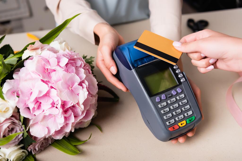 Vue recadrée du client payant avec carte de crédit par terminal dans les mains du fleuriste près hortensia floraison sur le bureau - Photo, image