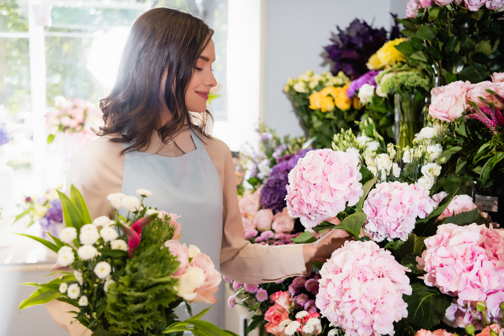 Florista sorridente com buquê tomando hortênsia na loja de flores com janela embaçada no fundo - Foto, Imagem
