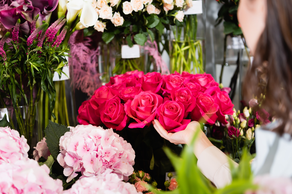 Обрізаний вид на жіночого флориста, який піклується про троянди на стійках квітів на розмитому фоні
 - Фото, зображення