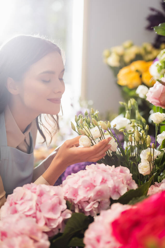 Щасливий флорист із закритими очима пахне квітами еустоми біля гортензії з розмитим вікном на фоні
 - Фото, зображення