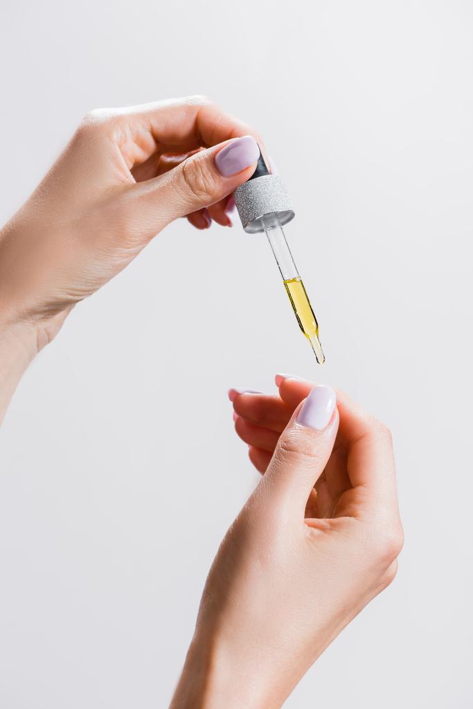 обрізаний вид жінки, що наносить олію з піпетки на нігті ізольовані на сірому
 - Фото, зображення