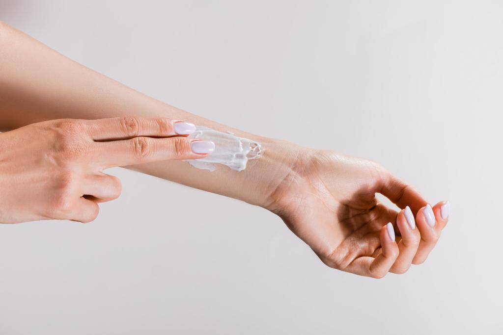 обрезанный вид женщины, наносящей крем для рук на руку, изолированный на сером - Фото, изображение