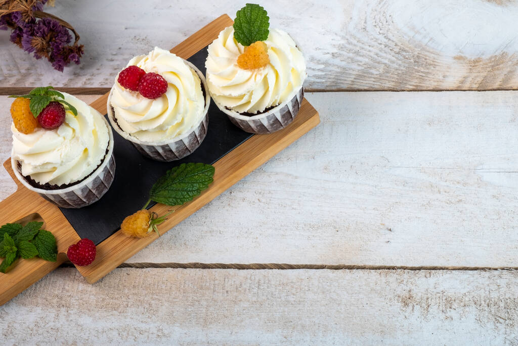 Σοκολατένια cupcakes με κρέμα τυριού και μούρα σε λευκό ξύλινο πιάτο. Άποψη από ψηλά. - Φωτογραφία, εικόνα