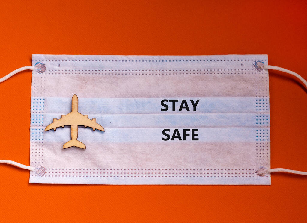A Coronavirus járattörlési koncepciója. Arc maszk és repülőgép játék narancssárga háttérrel. "Vigyázz magadra". Fénymásolási hely. - Fotó, kép