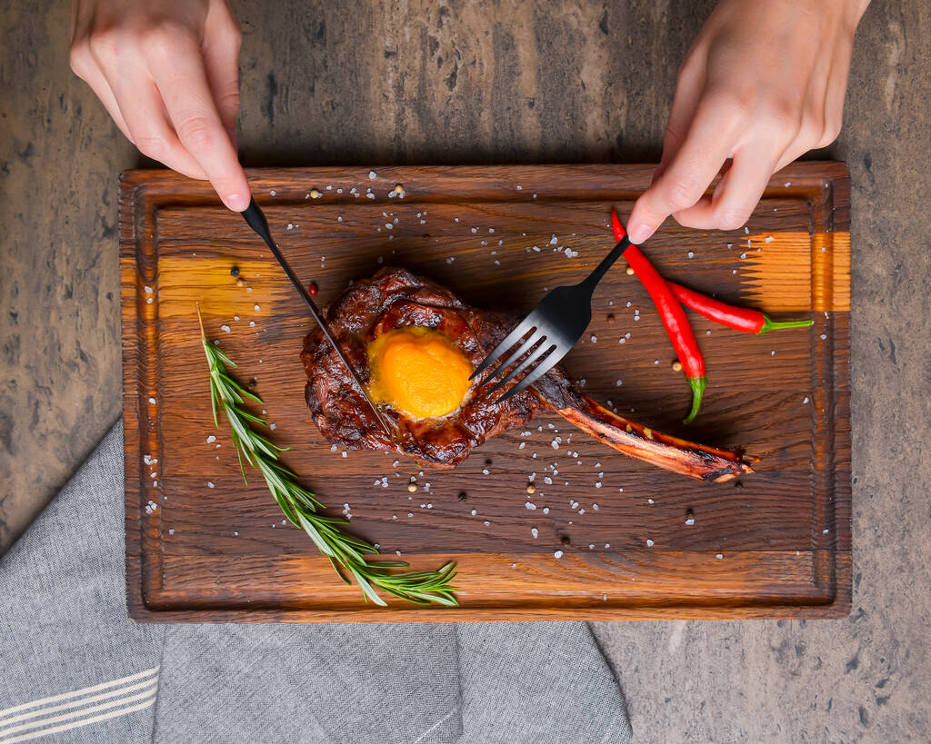 Grillezett tomahawk steak fűszerekkel, rusztikus fapadlón, fa háttér felett tálalva. Grill koncepció, grillezett hús steak, őszi szezonális étel. Steak késsel és villával. - Fotó, kép