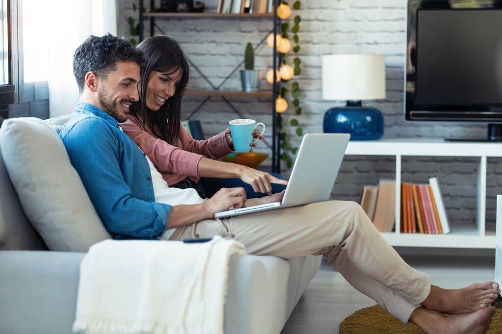 Съемка счастливой красивой пары с помощью компьютера, сидя на диване дома. - Фото, изображение