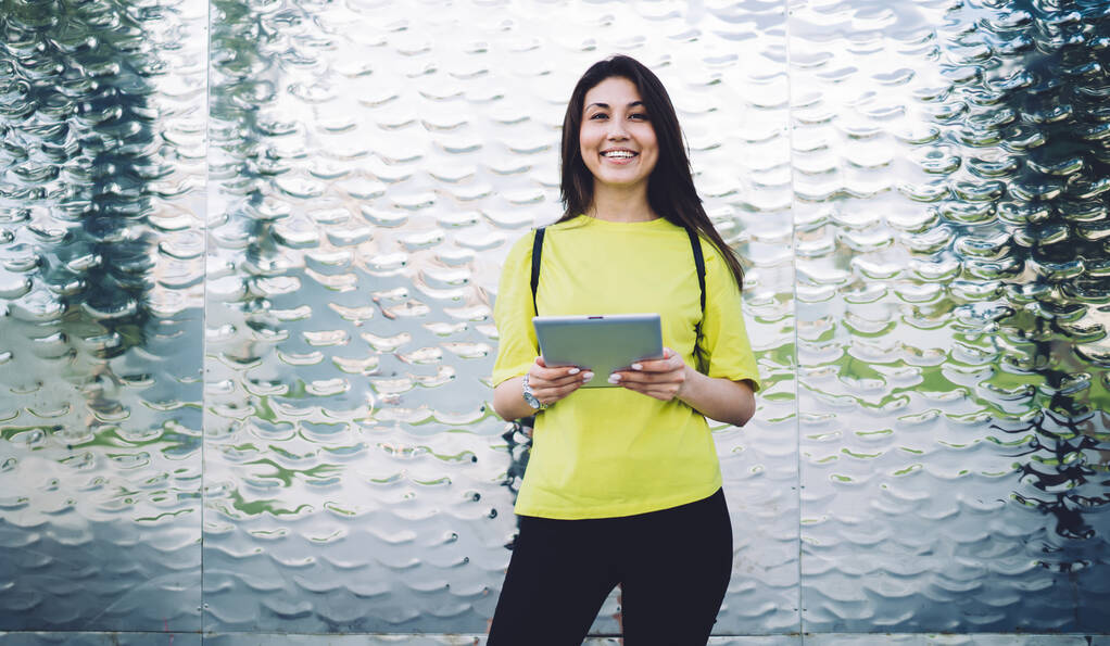 Μισού μήκους πορτρέτο του χαρούμενου ασιατικό θηλυκό στέκεται σε εξωτερικούς χώρους κρατώντας σύγχρονη ψηφιακή ταμπλέτα με σύνδεση 4G, γυναίκα χιλιετή φοιτητής απολαμβάνοντας σε απευθείας σύνδεση εκπαίδευση στο touchpad κοιτάζοντας κάμερα - Φωτογραφία, εικόνα