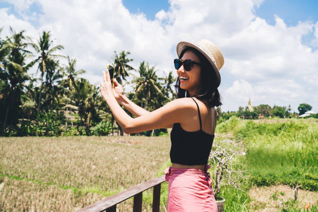 Смеющиеся женщины-путешественницы, пользующиеся мобильным телефоном для фотографирования тропического ландшафта и отворачивающиеся, наслаждаясь летними каникулами на Бали - Фото, изображение