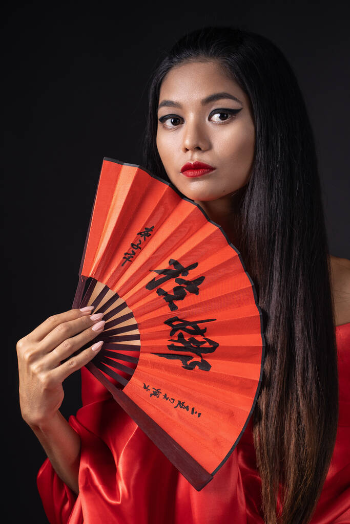 на чорному фоні китайська дівчина з червоними губами і в червоній традиційній китайській сукні. - Фото, зображення