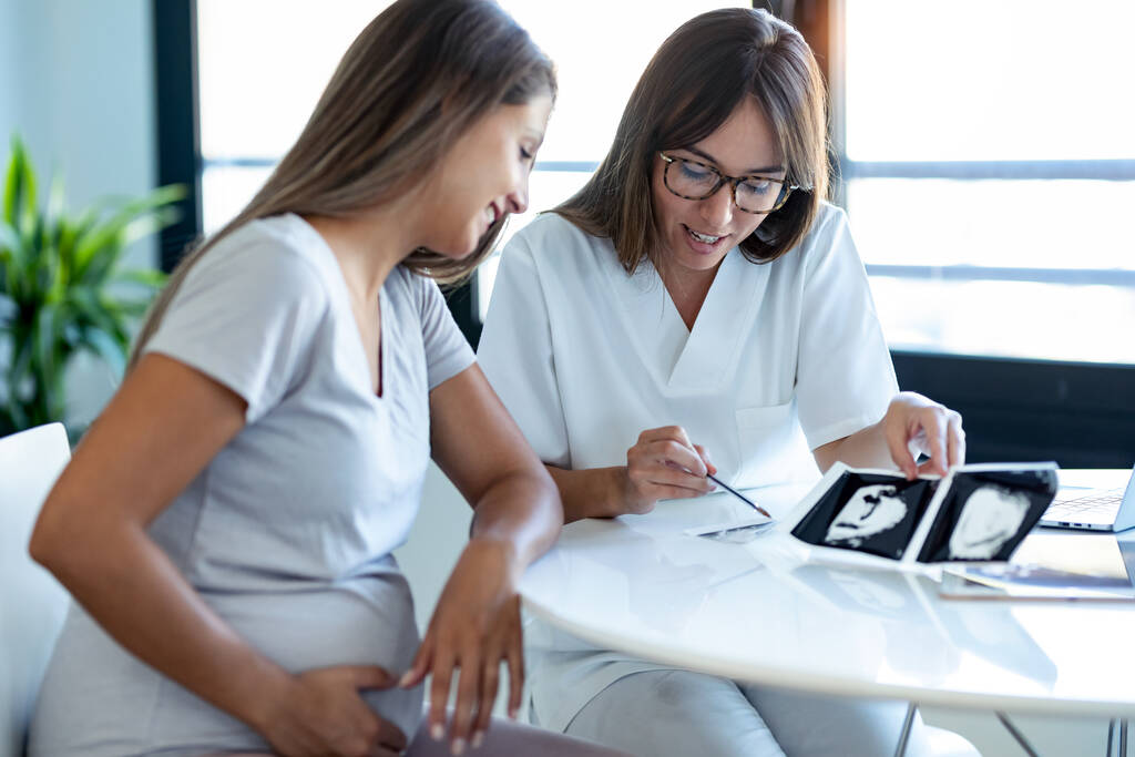 Inyección de médico ginecólogo mujer joven que muestra a la mujer embarazada ultrasonido bebé exploración en consulta médica. - Foto, imagen