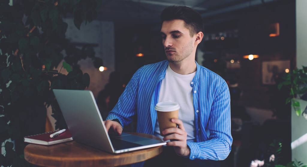 Valkoihoinen mies IT ammatillinen tarkkailun ohjelma tekstiä moderni kannettava tietokone tekee etätyötä kahvilassa, komea mies takeaway cup katsella verkossa web webinar kautta sovellusalusta - Valokuva, kuva