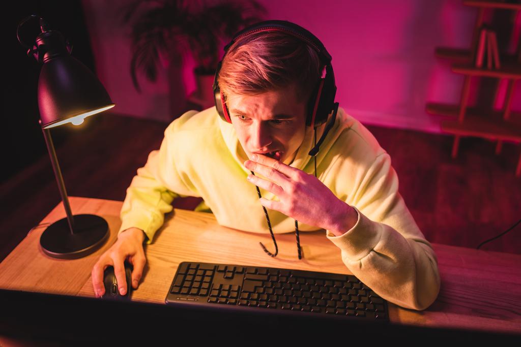 Jugador nervioso en auriculares usando computadora en primer plano borroso  - Foto, Imagen