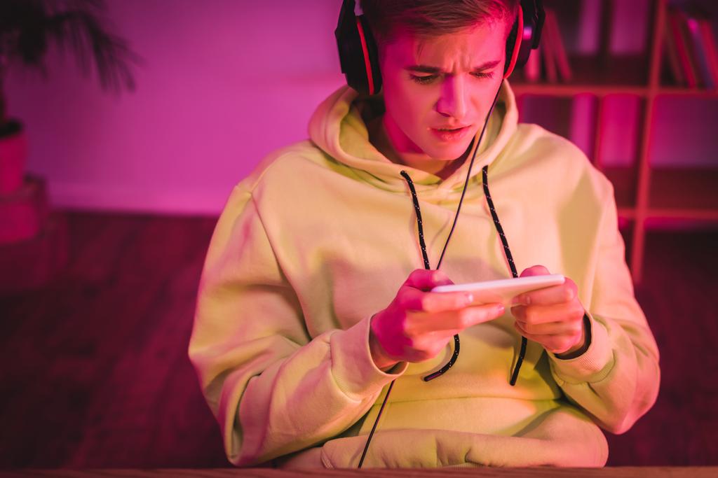 Worried gamer in headphones using smartphone at home  - Photo, Image