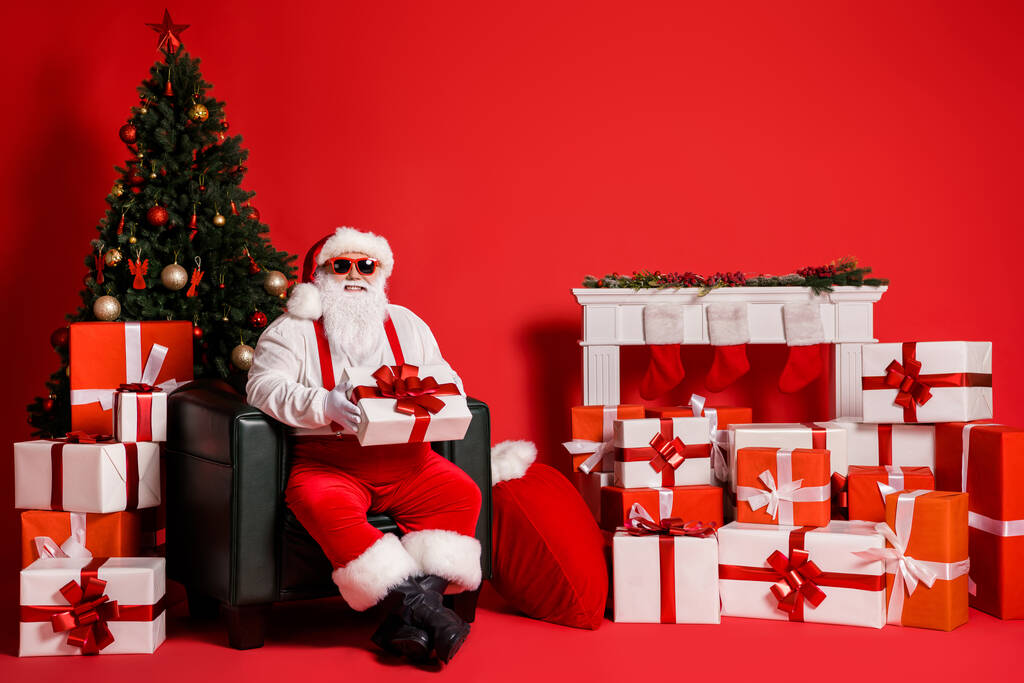 Muotokuva hänen hän mukava houkutteleva funky rasvaa iloinen iloinen iloinen Santa isä istuu nojatuoli tilalla käsissä antaa lahja toimitus kasa eristetty kirkas eloisa paistaa elinvoimainen punainen väri tausta - Valokuva, kuva