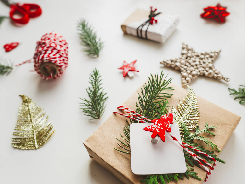 Weihnachtsgeschenke in Bastelpapier mit Tannenzweigen verpackt. Rote Dekorationen in Form eines Weihnachtsbaums. Neujahrsgeschenke. Feierlicher Hintergrund. Winterurlaubsstimmung. - Foto, Bild