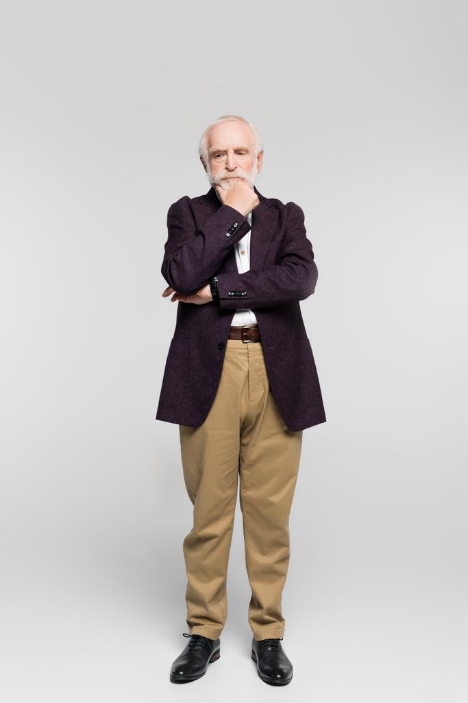 Aggressiver Senior schaut weg, während er auf grauem Hintergrund steht - Foto, Bild