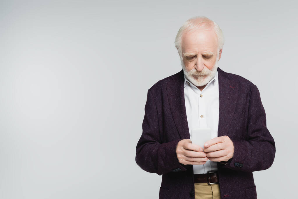 Ηλικιωμένος άνδρας με πουκάμισο και σακάκι χρησιμοποιώντας smartphone απομονωμένο σε γκρι  - Φωτογραφία, εικόνα