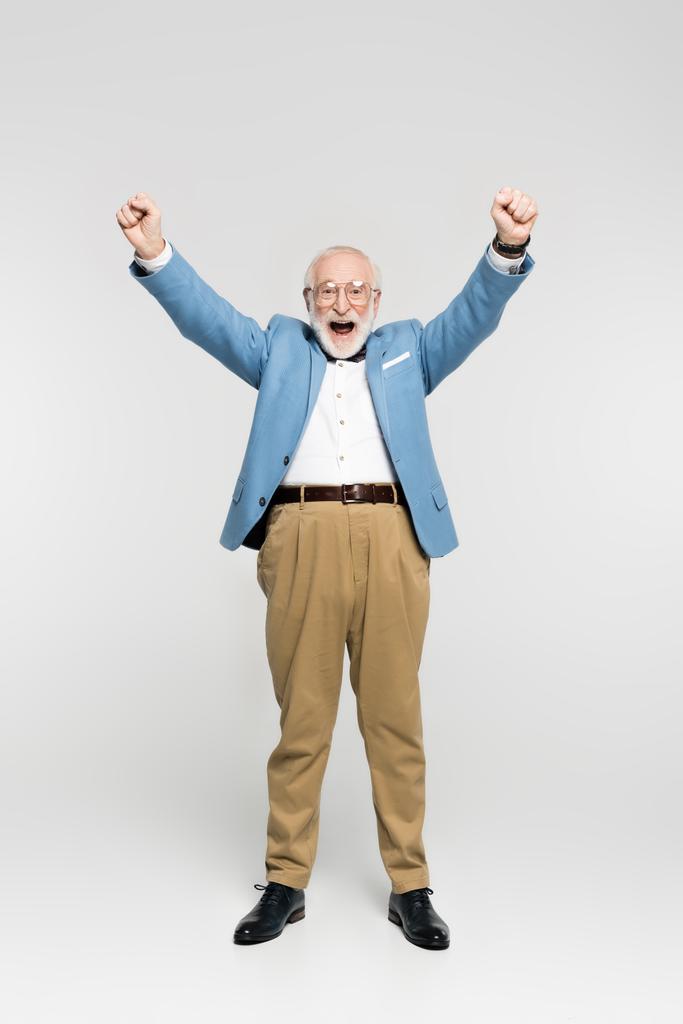 Hombre mayor excitado en chaqueta azul y anteojos mostrando sí gesto sobre fondo gris  - Foto, imagen