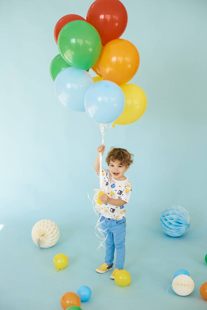 Portrait pleine longueur d'un garçon joyeux tenant des ballons posant sur fond bleu - Photo, image
