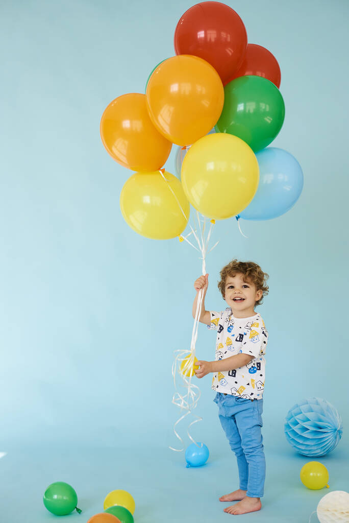Plně dlouhý portrét veselého chlapce držícího balóny pózující na modrém pozadí - Fotografie, Obrázek