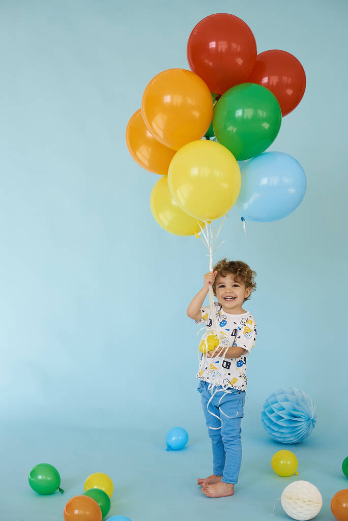 Ganztägiges Porträt eines fröhlichen Jungen mit Luftballons vor blauem Hintergrund - Foto, Bild
