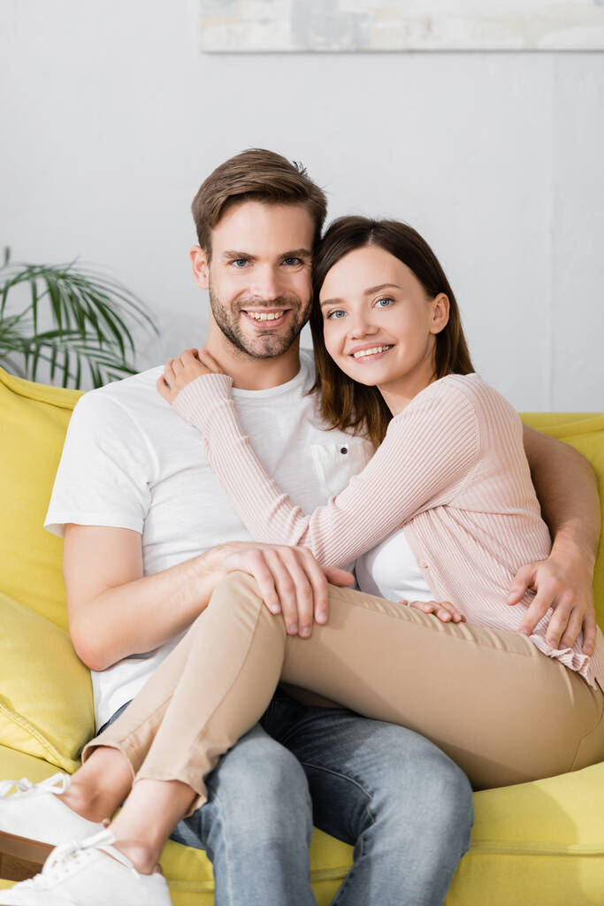 fröhliche Männer und Frauen, die sich zu Hause auf dem Sofa umarmen - Foto, Bild