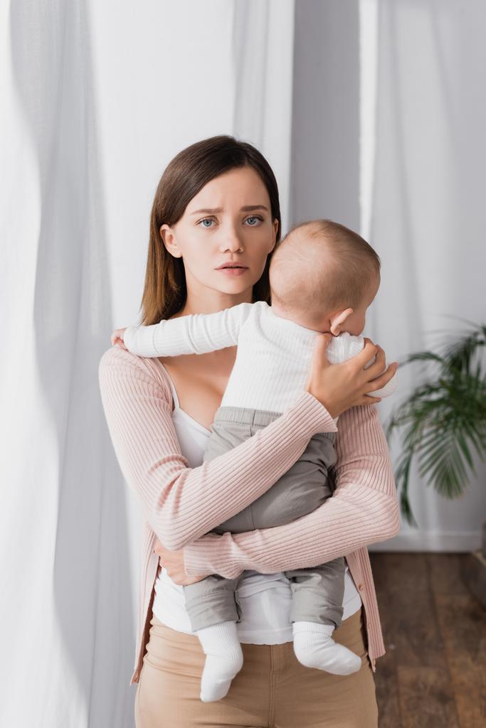 mujer preocupada sosteniendo en brazos bebé niño y mirando a la cámara - Foto, imagen