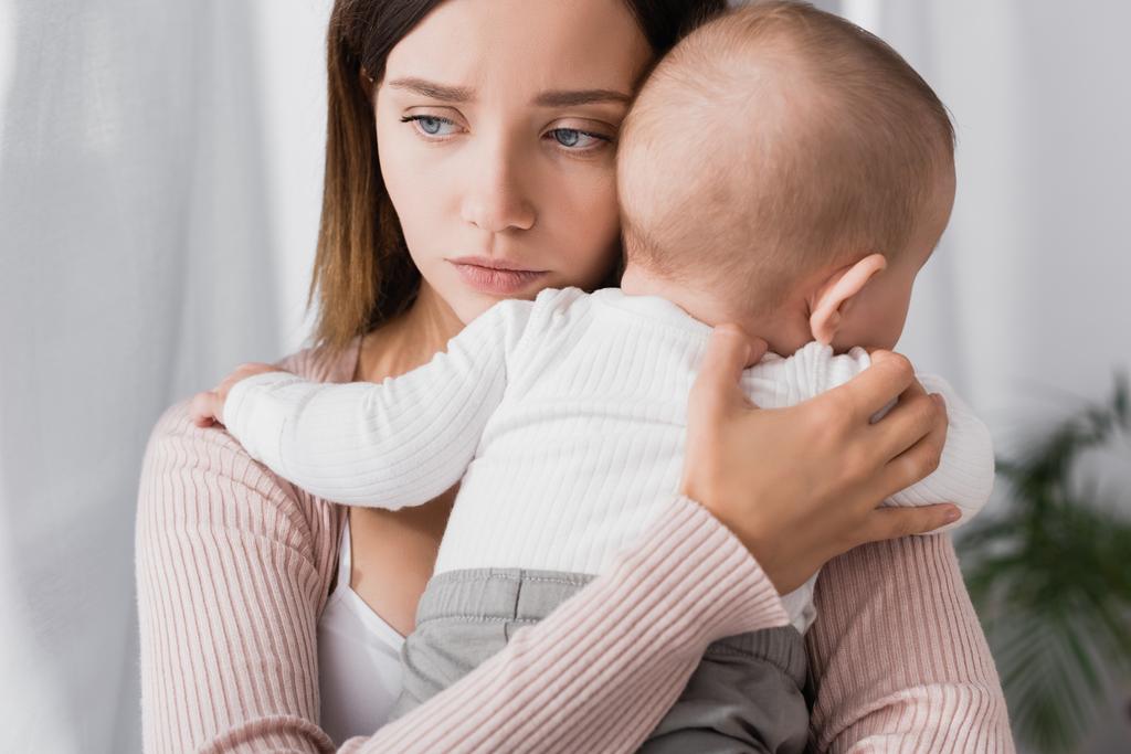 беспокойная мать держит в руках ребенка мальчика и смотрит в сторону - Фото, изображение
