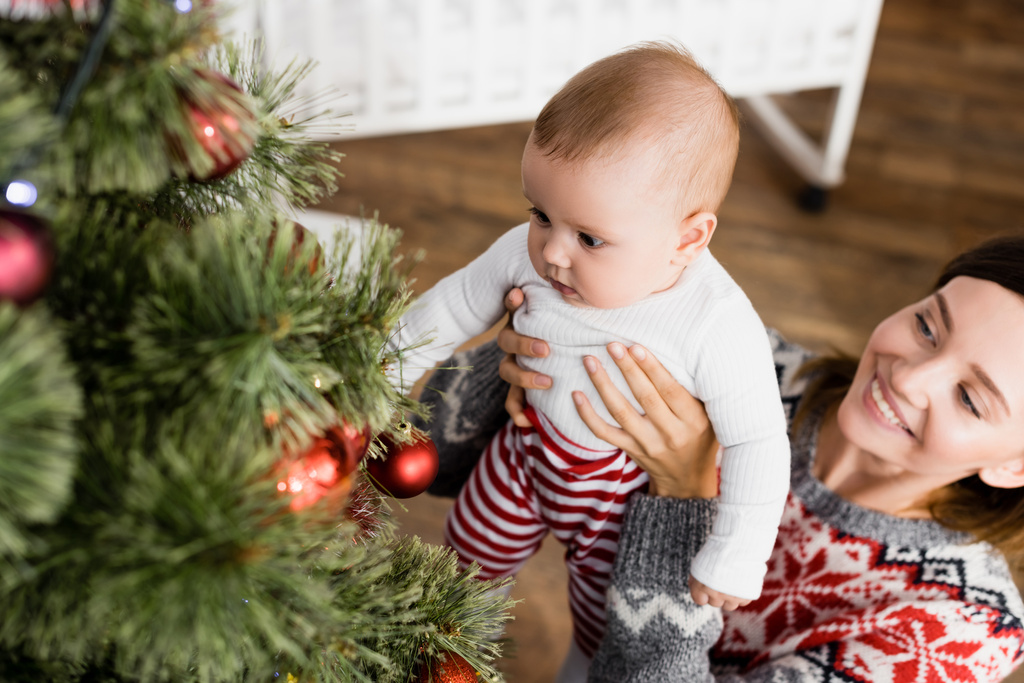 Mutlu bir kadın kollarını tutuyor. Süslü Noel ağacının yanında bir oğlan çocuğu. - Fotoğraf, Görsel