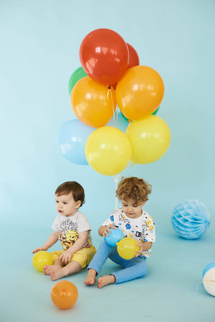 Mavi arka planda balonlar tutan iki neşeli çocuğun tam boy portresi. - Fotoğraf, Görsel