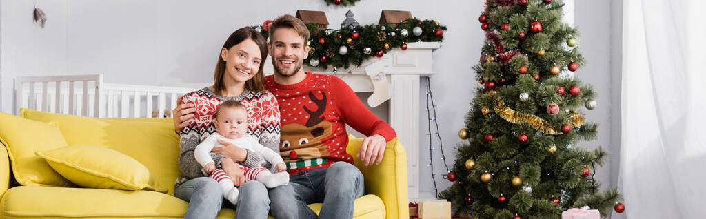 クリスマスツリーの近くのソファに座っている男の子と幸せな家族 - 写真・画像