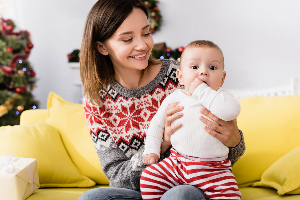 Fröhliche Frau im Pullover hält Säugling im Arm  - Foto, Bild
