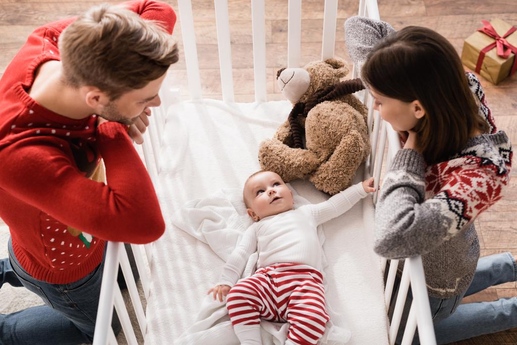 high angle view of parents standing on knees and looking at baby boy in crib  - Photo, Image