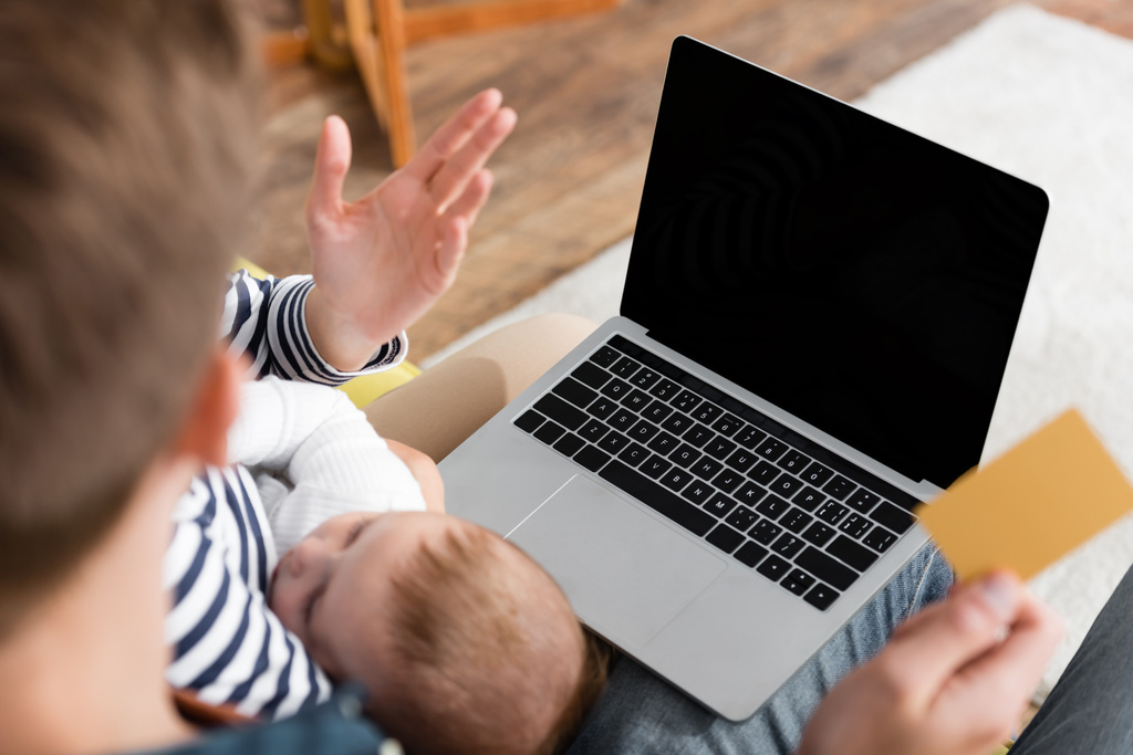 Laptop mit leerem Bildschirm in der Nähe von Säugling schlafend in der Nähe von Eltern Online-Shopping auf verschwommenem Vordergrund  - Foto, Bild