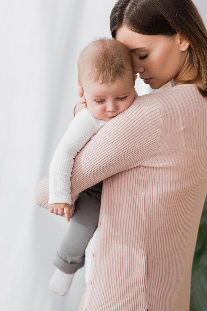 matka trzyma w ramionach podczas uspokajania zdenerwowanego syna niemowlęcia  - Zdjęcie, obraz
