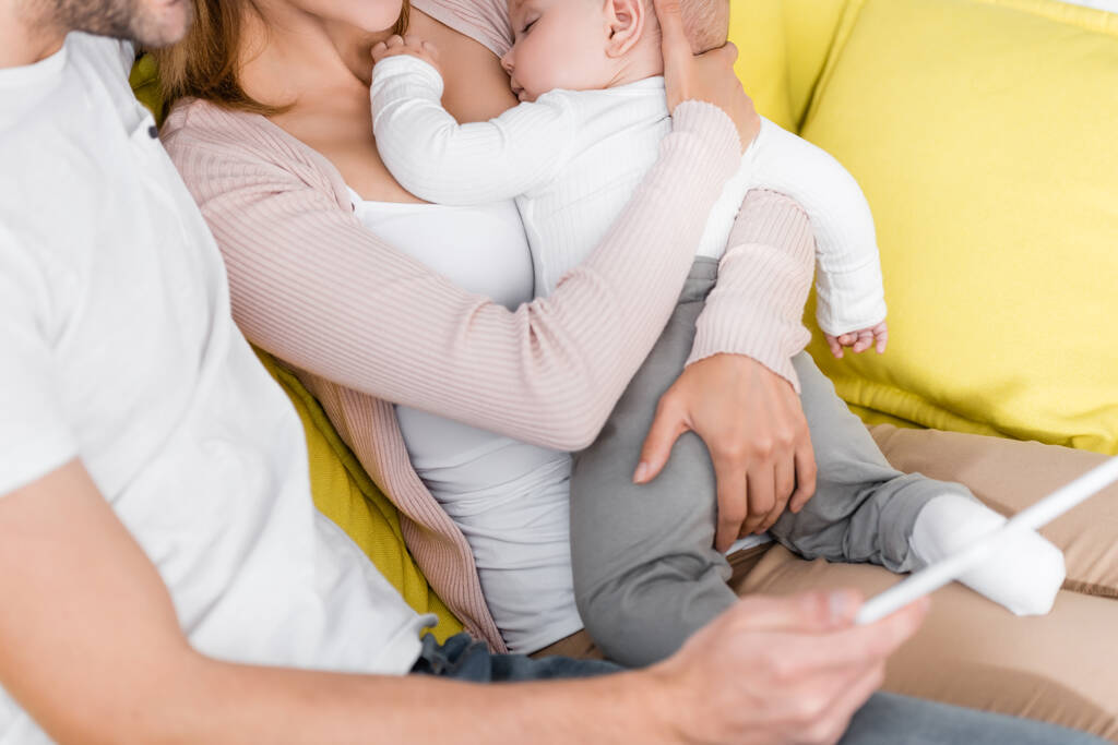 Mann mit digitalem Tablet neben Frau hält schlafenden Säugling im Arm  - Foto, Bild
