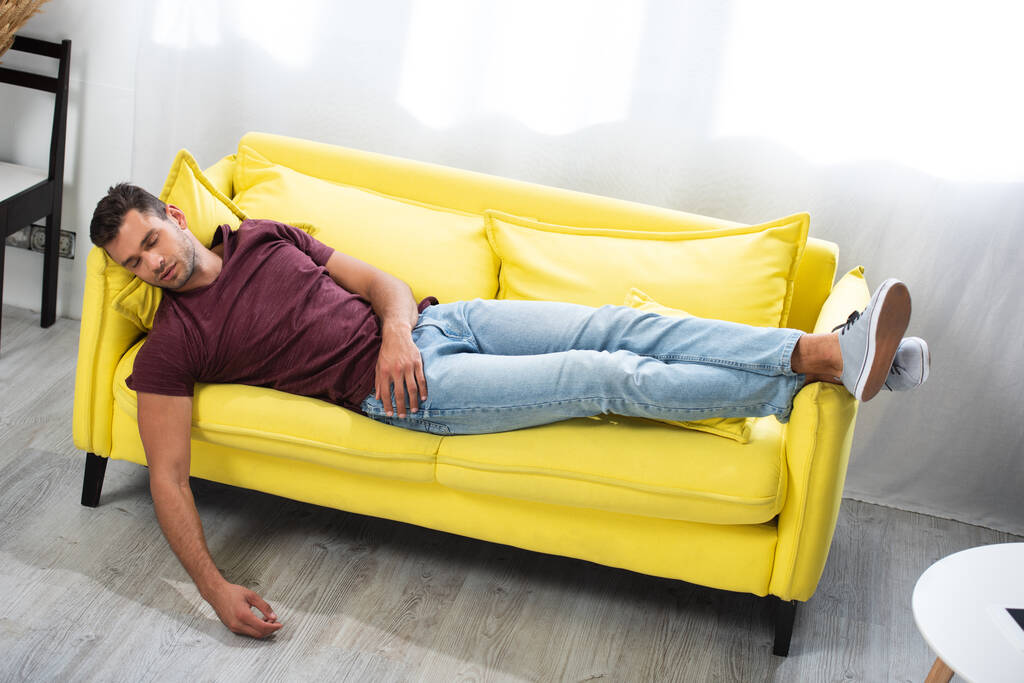 Νεαρός κοιμάται ενώ ξαπλώνει στον καναπέ στο σπίτι  - Φωτογραφία, εικόνα
