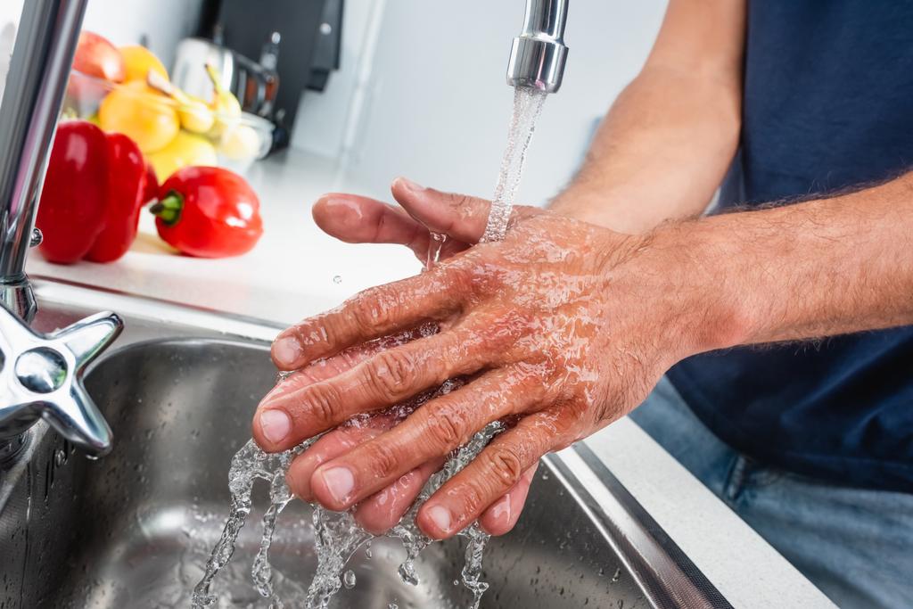 Cropped view of man washing hands in kitchen near vegetables on blurred background  - Foto, imagen